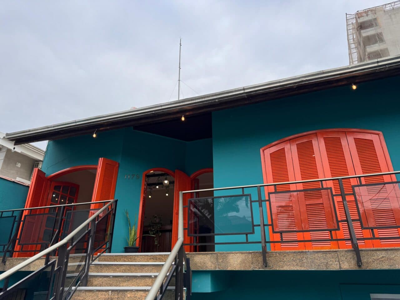 Fachada turquesa do Meraki Hostel com janelas laranja